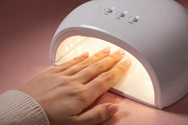 Close-up of a hand being cured under a glowing white LED nail lamp