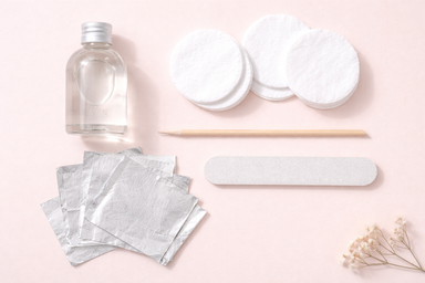 Flat lay of nail removal supplies arranged neatly on a blush pink surface 