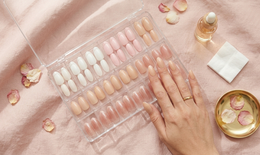 elegant flat-lay featuring a clear acrylic storage case with rows of pristine press-on nails arranged neatly in individual compartments — almond-shape press-ons in various neutral shades