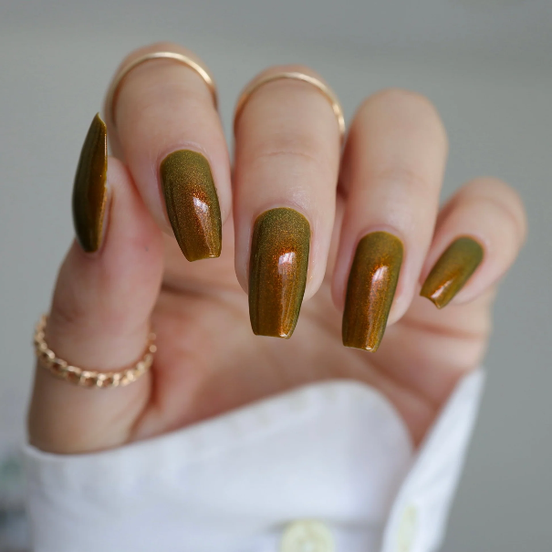 Brown chrome nails — long coffin nails in a bronze-brown color-shift chrome polish that flashes copper and olive-gold in the light, with gold rings and a white sleeve